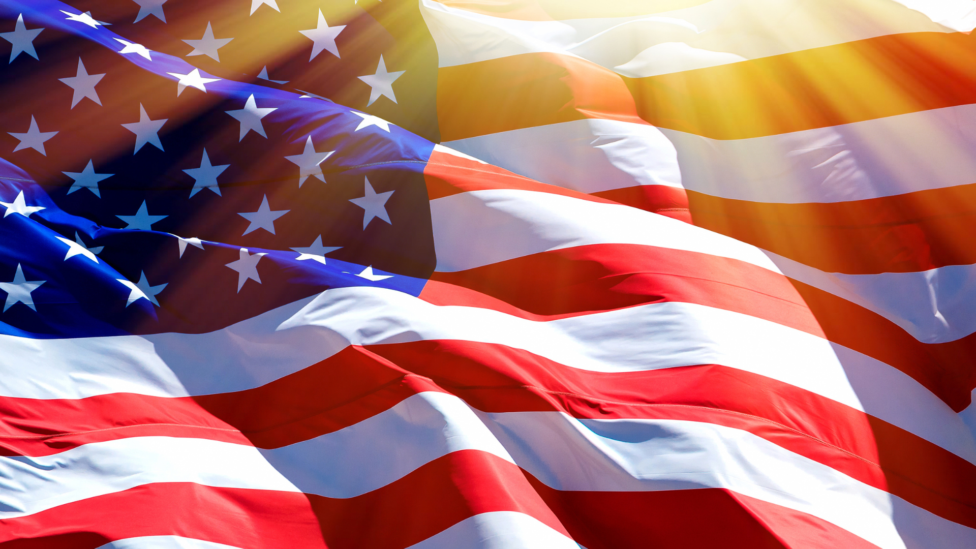 Close up Photo of the American Flag waving in the wind with the sun shining over top. 