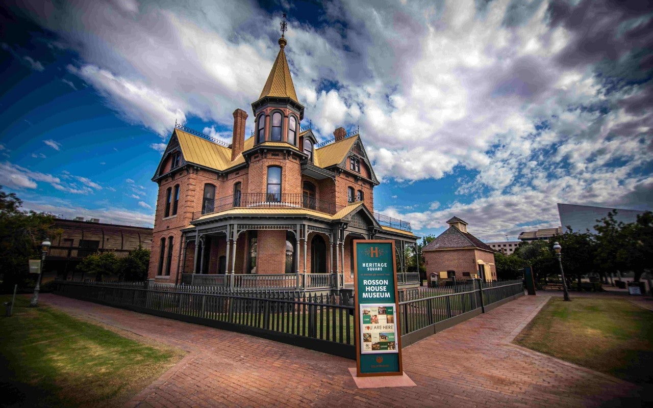 A victorian-style house in front of a blue sky. A sign in front of the house identifies it as "ROSSON HOUSE MUSEUM".