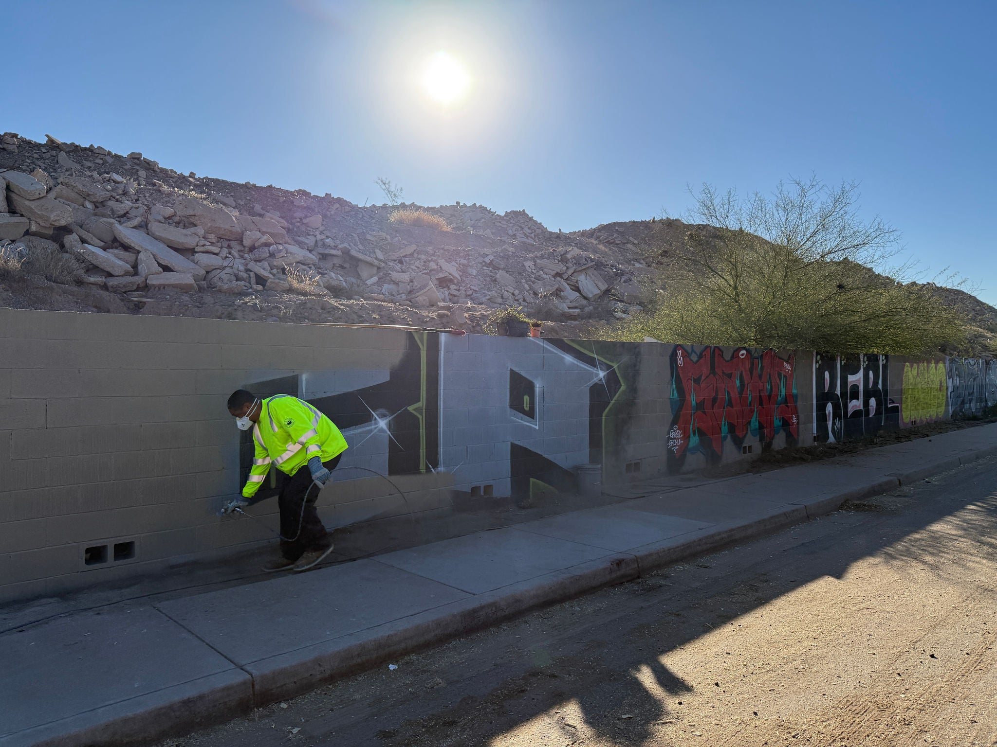 a graffiti buster crewmember painting a block fence to cover graffiti
