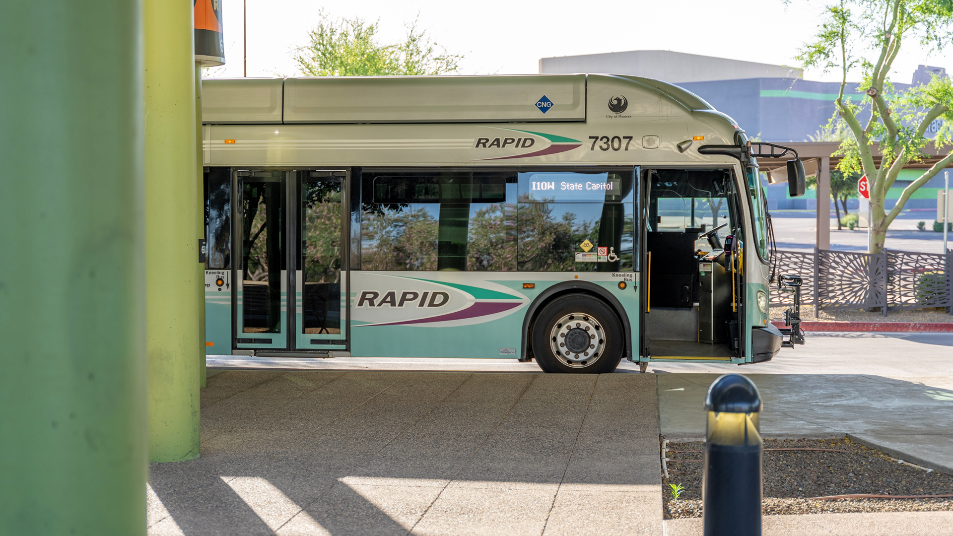 A City of Phoenix RAPID bus stopped at the Desert Sky Transit Center in the background in focus, with green pillars on the left side of the image. 