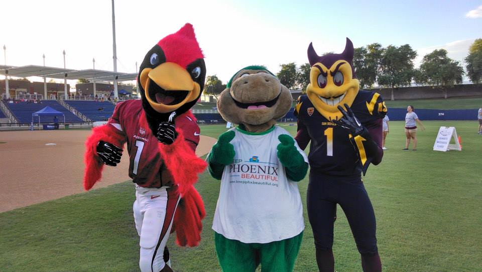 Recylesaurus. a green dinosaur mascot, stands between the Arizona Cardinals mascot, Big Red, and the ASU Sun Devils mascot, Sparky.