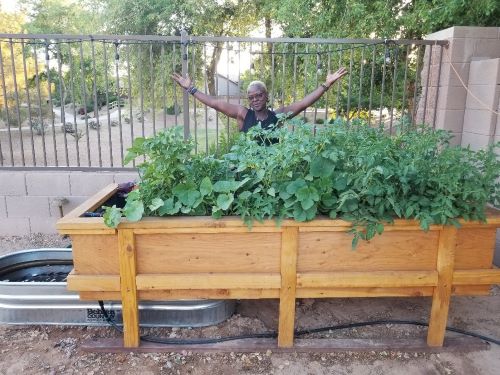 The same program participant stands behind their Lehr garden system, which is now fully bloomed.