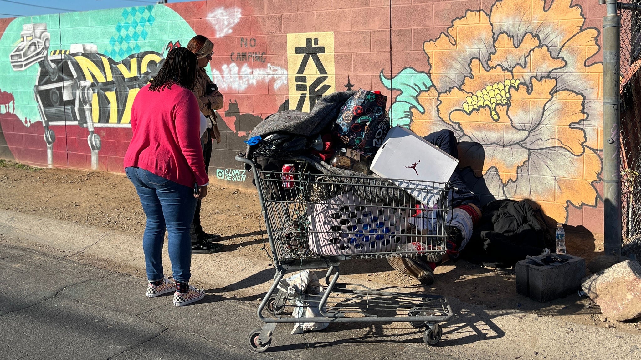 Two homeless liaisons speak to a person behind a shopping cart.
